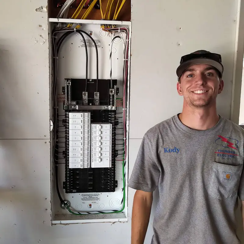 Thunder Electric electrician Kody in an Est. 1974 company shirt beside a freshly wired residential breaker panel